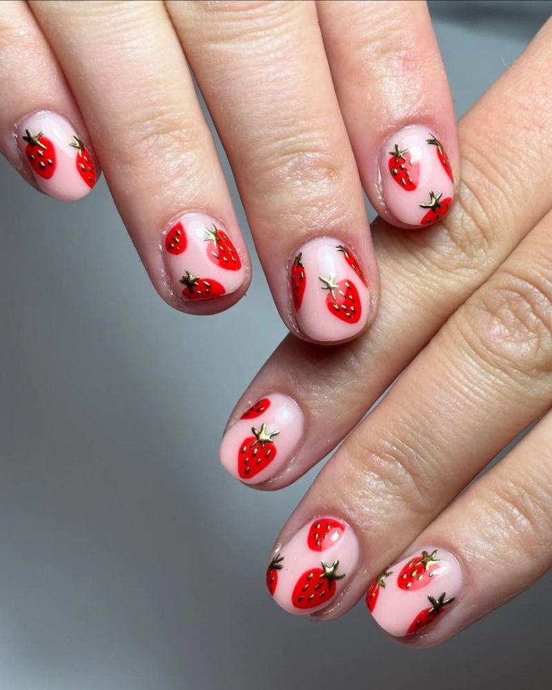 Ongles courts nude avec nail art fraise rouge et accents dorés