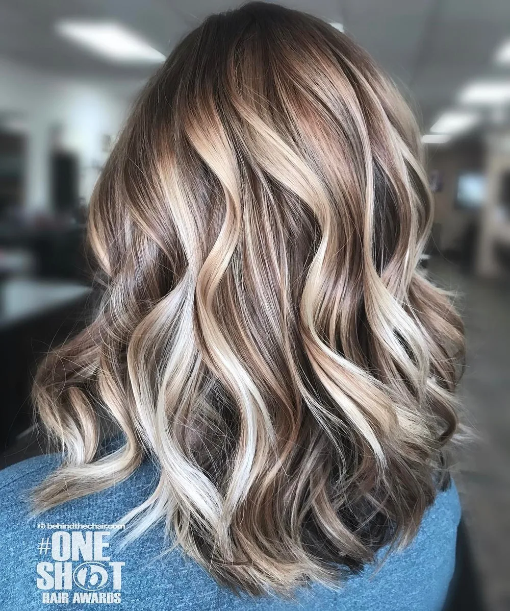 Balayage blond foncé et mèches platine multi-tons sur longueurs ondulées