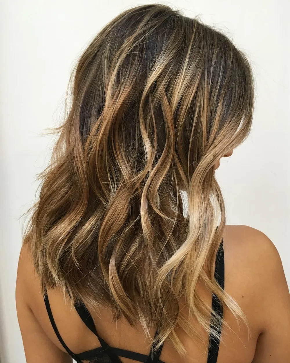 Balayage tissant des rubans de blond miel dans une base brune, effet fils dorés