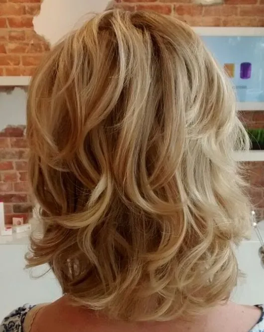 Cheveux mi-longs bouclés blond doré coupés en couches