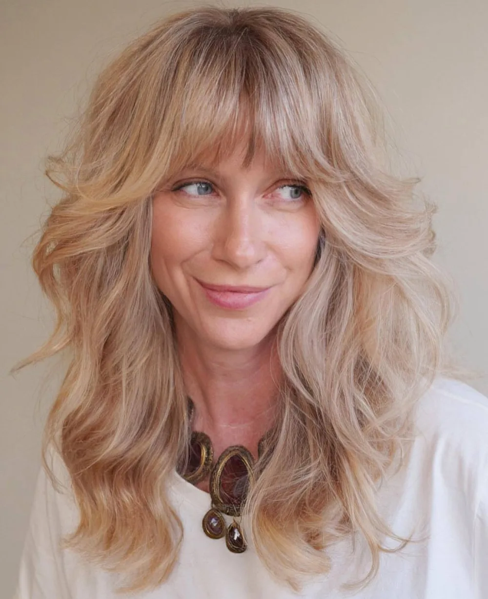 Shag blond volumineux avec frange plumeuse encadrant le visage