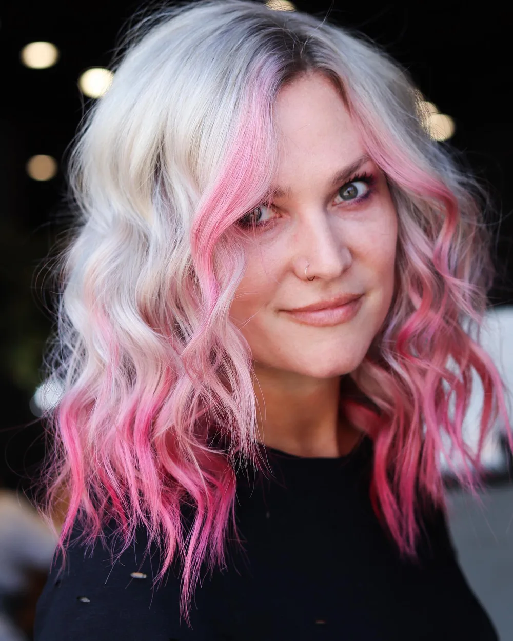 Blonde avec mèches rose œillet et boucles souples, coupe mi-longue
