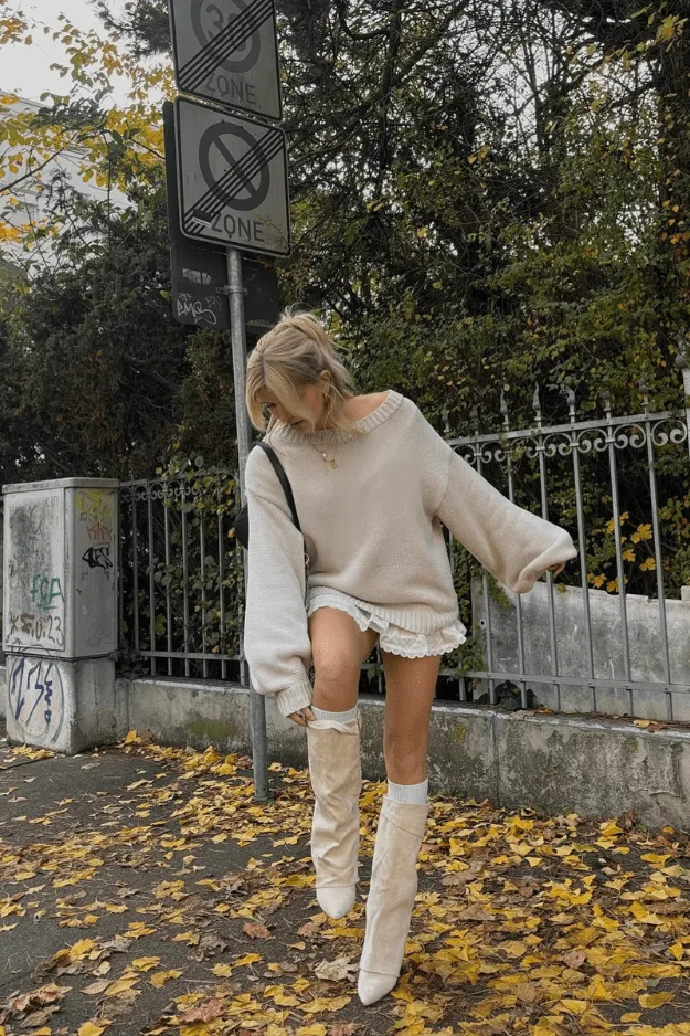 Bottes hautes en cuir crème portées avec pull et short sous les feuilles d'automne, tendance 2026