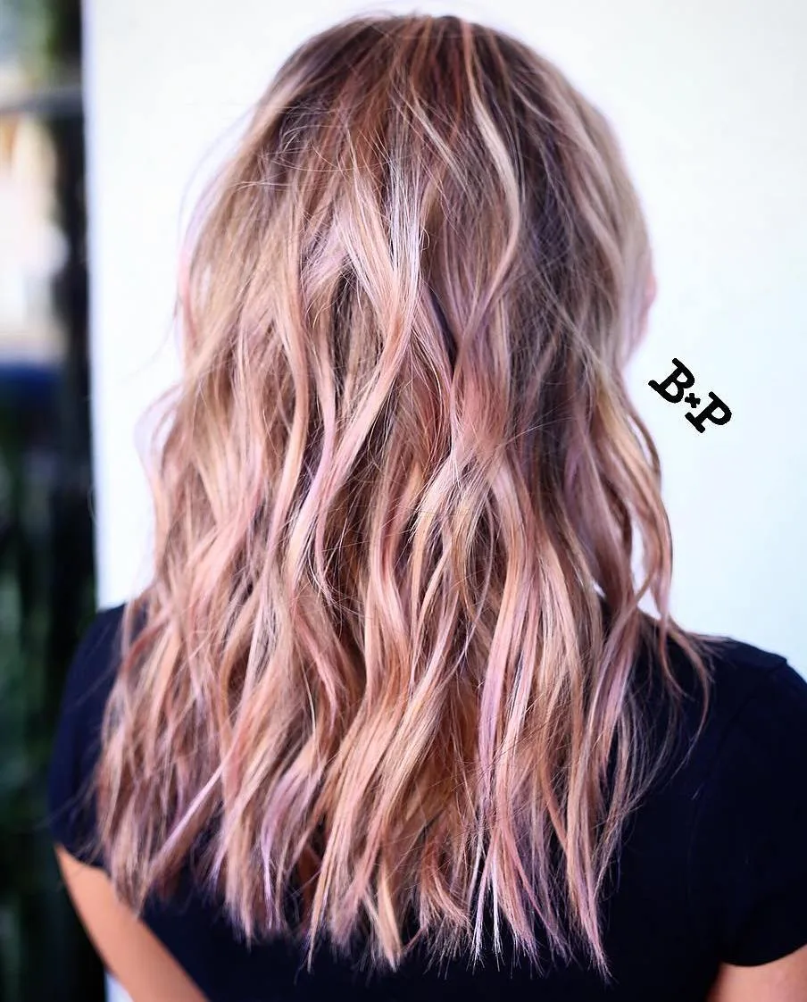 Cheveux bronde avec mèches rose blush subtiles fondues sur ondulations