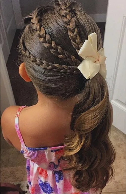 Coiffure petite fille avec triple tresse réunie en demi-queue latérale et nœud
