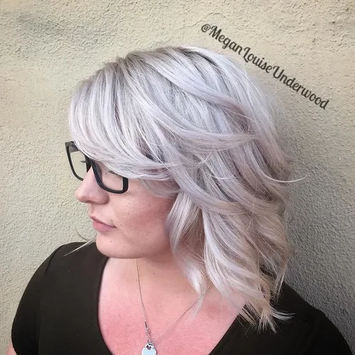 Coupe mi-longue blond argenté aux boucles souples et frange de côté pour visage carré