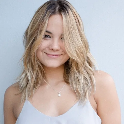 Coupe mi-longue blond doré dégradée et ondulée adoucissant un visage carré