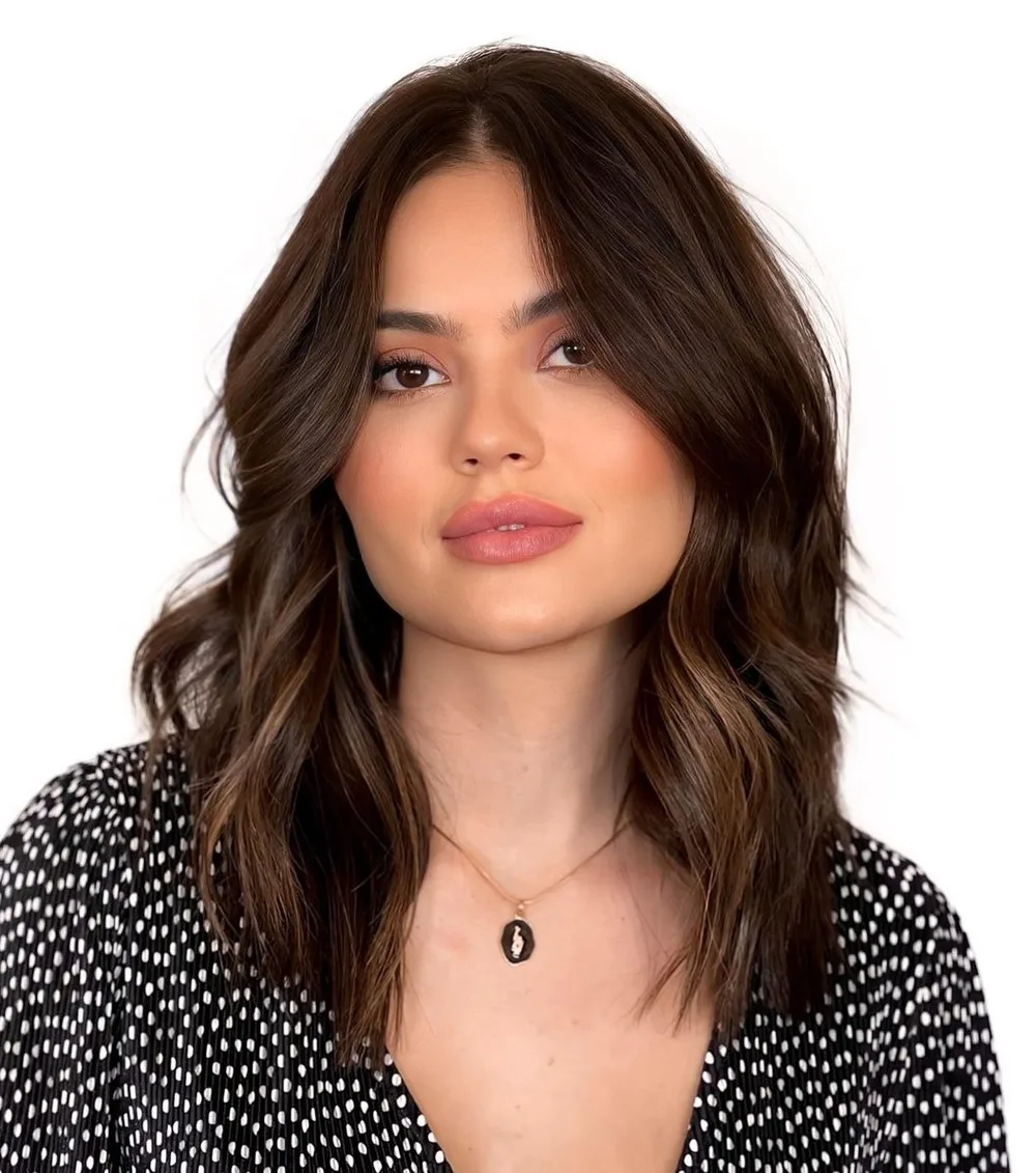 Coupe mi-longue brune ondulée avec frange rideau encadrant un visage carré