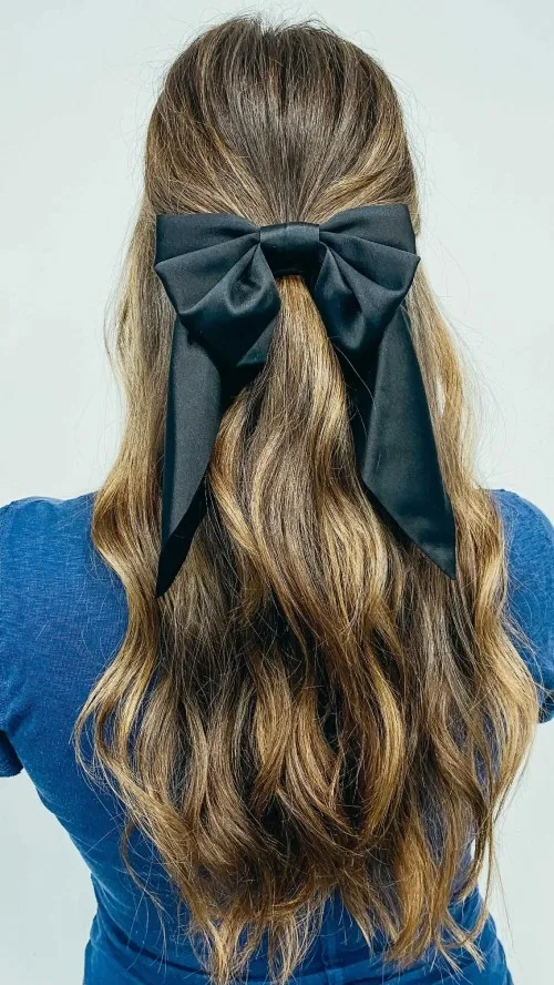 Demi-attache haute ornée d'un nœud noir en satin sur cheveux longs blonds