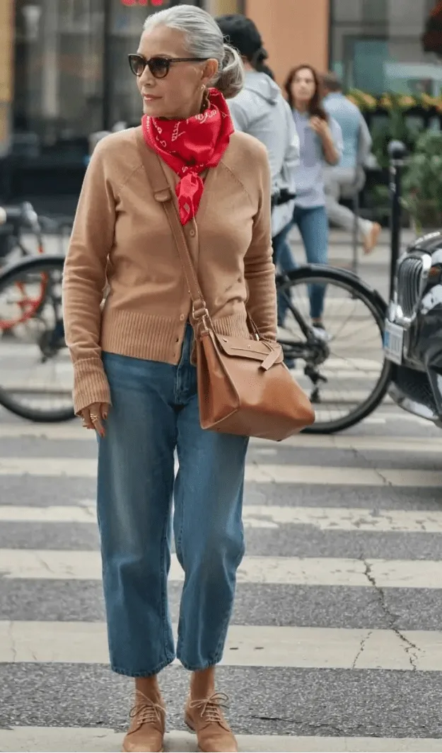 Femme de plus de 50 ans en jean droit avec pull camel et foulard rouge, style automne moderne