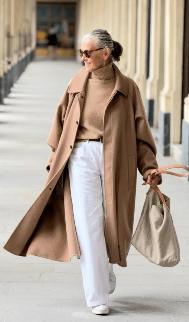 Femme de plus de 50 ans en manteau camel statement sur base neutre, style automne chic