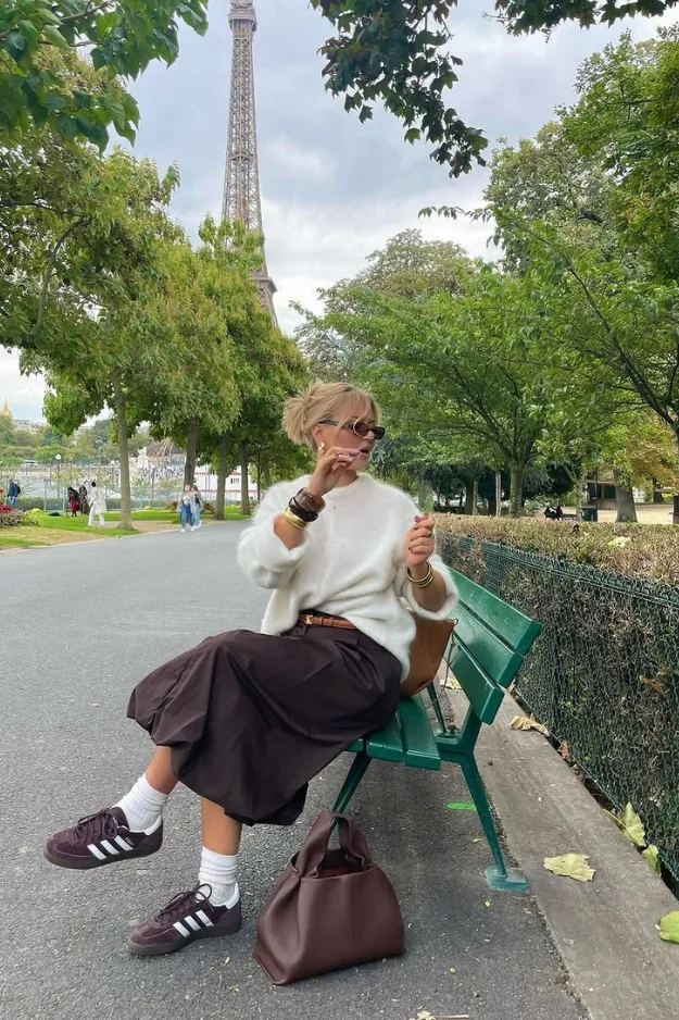 Femme en cardigan crème et jupe longue marron sur un banc parisien