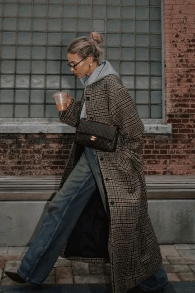 Femme en long manteau statement à carreaux porté sur un jean, tendance automne 2026