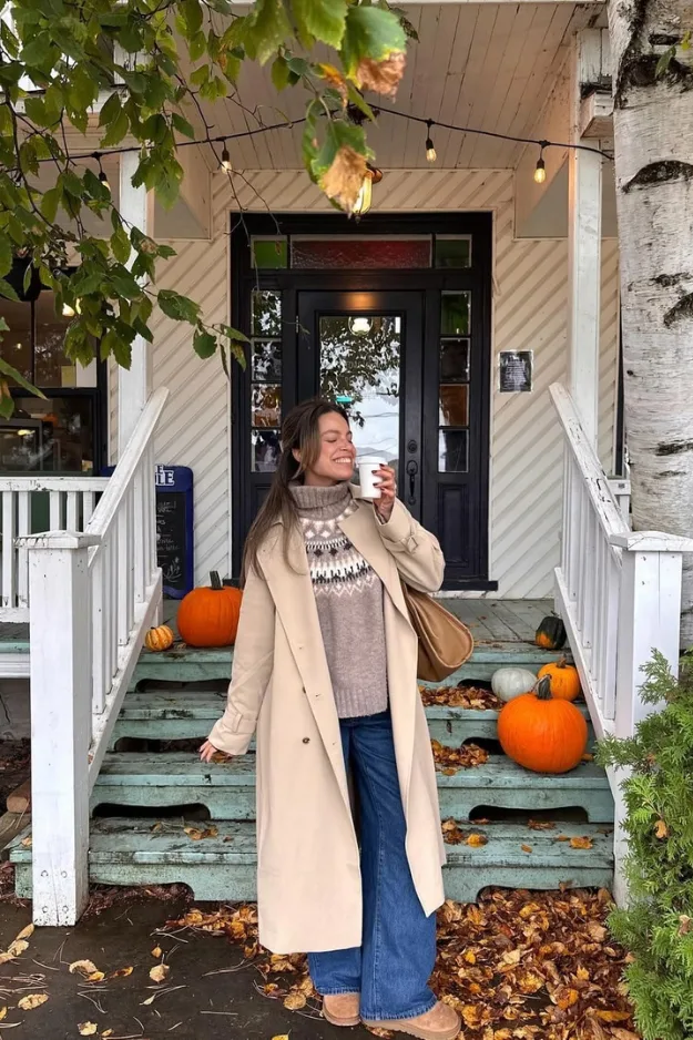 Femme en manteau long crème avec pull jacquard et jean flare, décor citrouilles