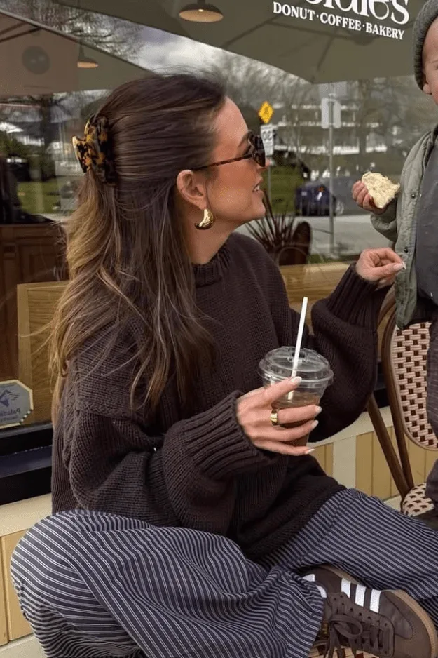 Femme en pull chocolat avec pantalon à fines rayures, boisson glacée en main