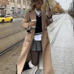 Femme en trench beige classique avec pull crème et bottines, look automne pluvieux