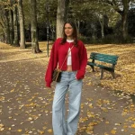 Femme en veste rouge avec jean clair et bottes, dans un parc aux feuilles d'automne