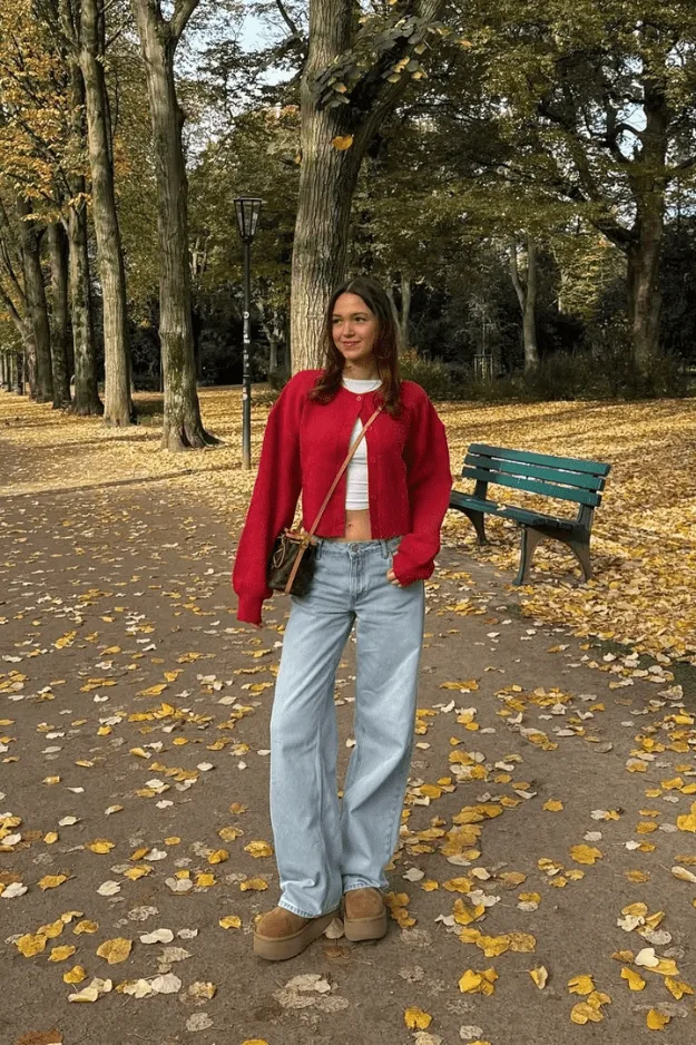 Femme en veste rouge avec jean clair et bottes, dans un parc aux feuilles d'automne