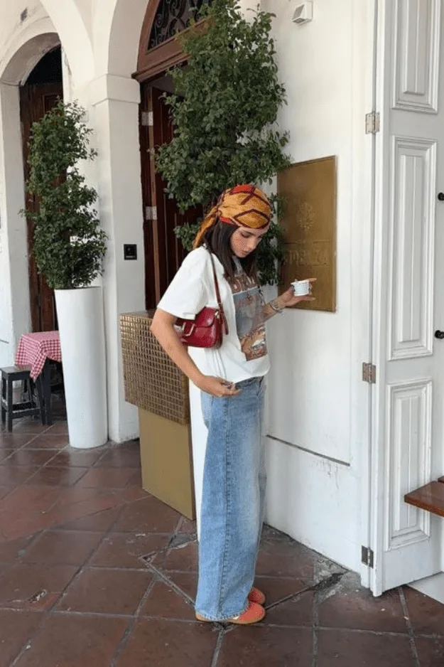 Jean large clair porté avec un tee graphique et un foulard de soie orange