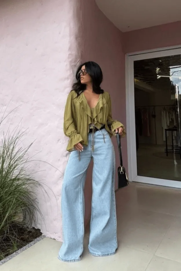 Jean large clair porté avec une blouse verte à volants ceinturée