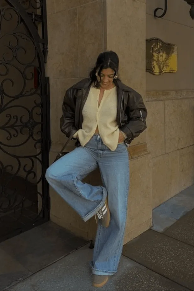 Jean large porté avec un bomber en cuir marron et un cardigan crème