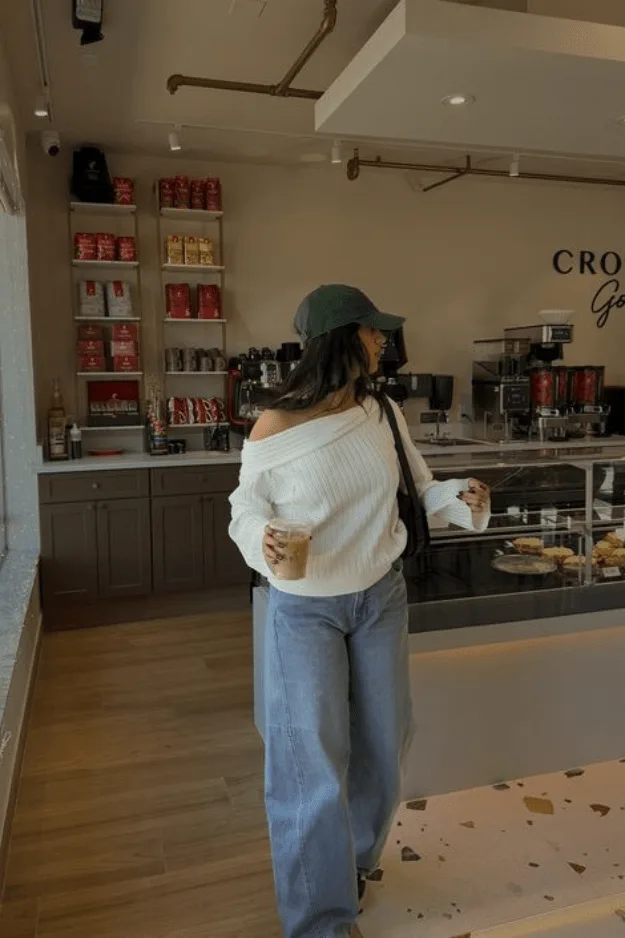 Jean large porté avec un gros pull blanc à épaule dénudée et une casquette verte