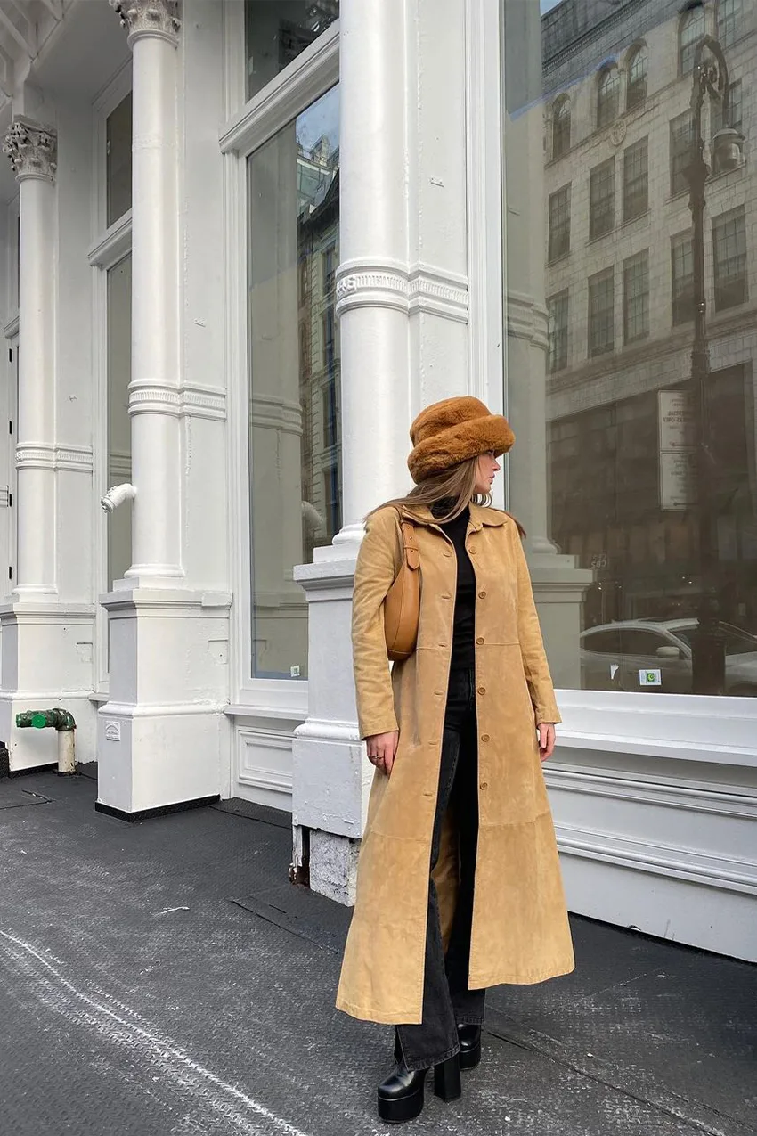 Long manteau camel porté sur un total look noir et des bottes