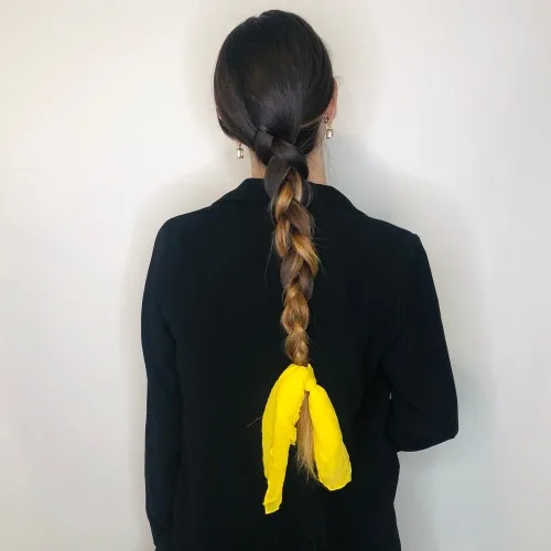Longue tresse agrémentée d'un foulard jaune noué aux pointes