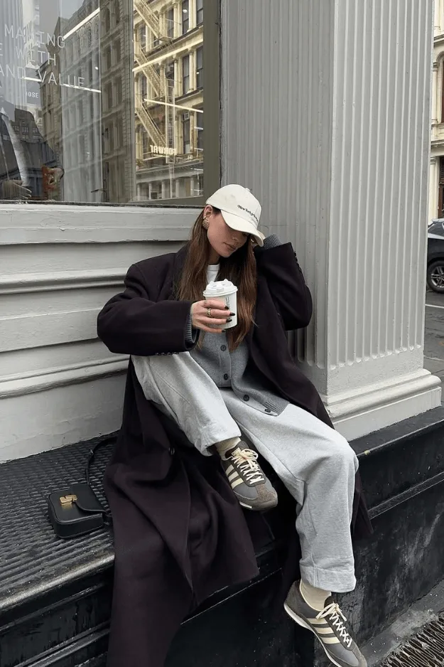 Look blazer oversize noir avec pantalon large gris, sneakers beiges et casquette blanche