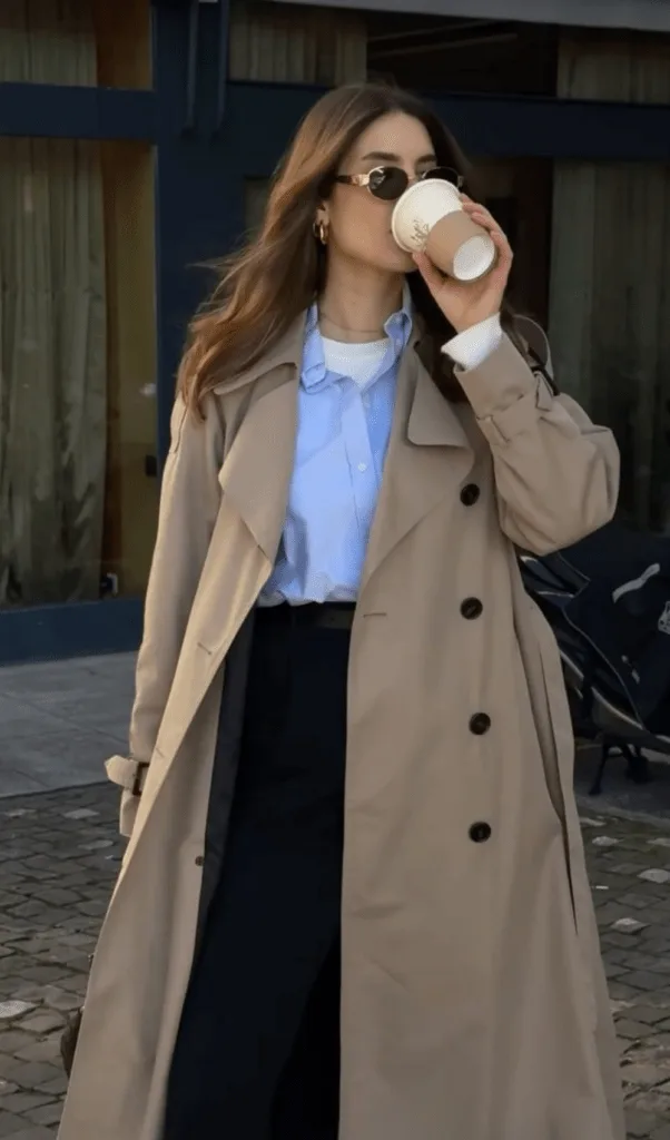 Look trench beige ouvert sur chemise bleu clair et pantalon noir avec café