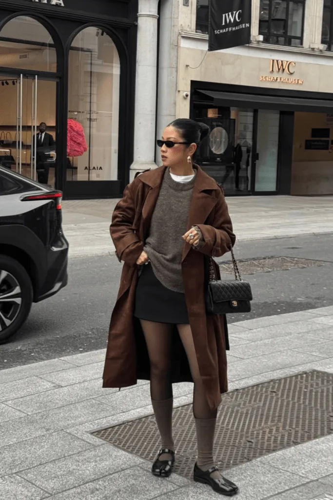 Look trench marron sur mini-jupe avec collants et bottines