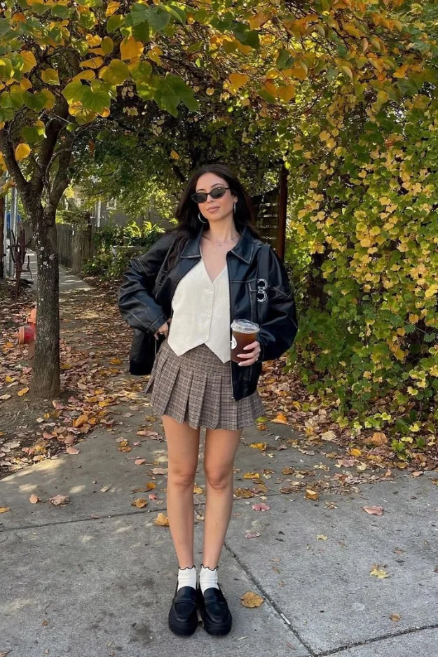 Look veste noire avec gilet crème et mini-jupe plissée grise, style Y2K preppy