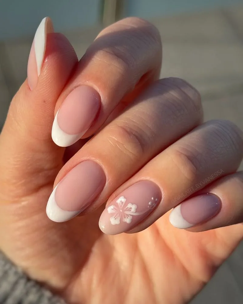Manucure french blanche avec fleur d'hibiscus blanche sur ongles amande, lumière dorée