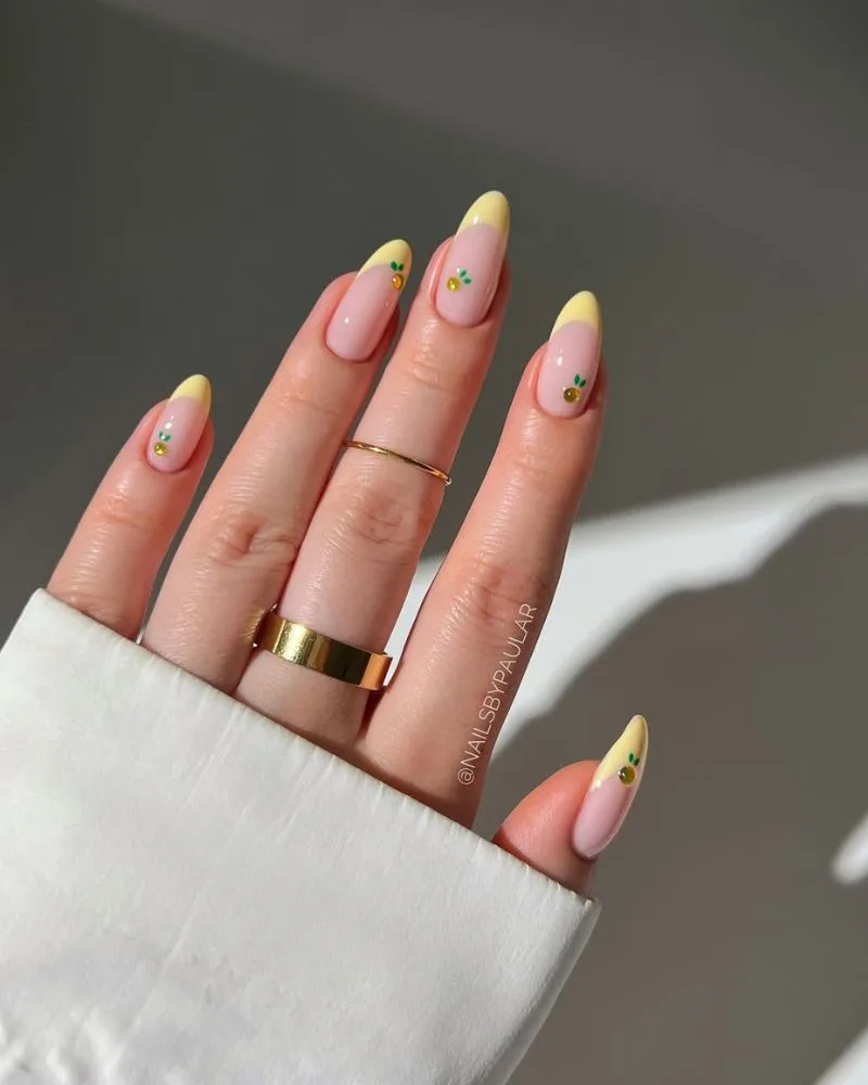 Manucure french jaune beurre avec petits agrumes orange et feuilles vertes minimalistes