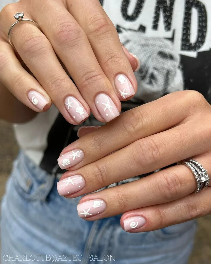 Ongles base nude avec nail art blanc minimaliste étoiles de mer et coquillages