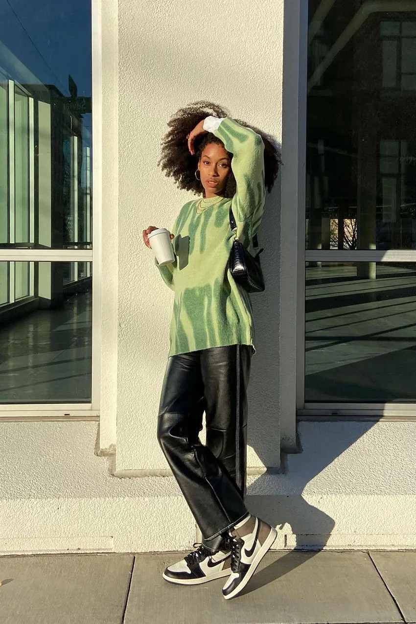 Pantalon en cuir porté avec un gros pull vert et des baskets