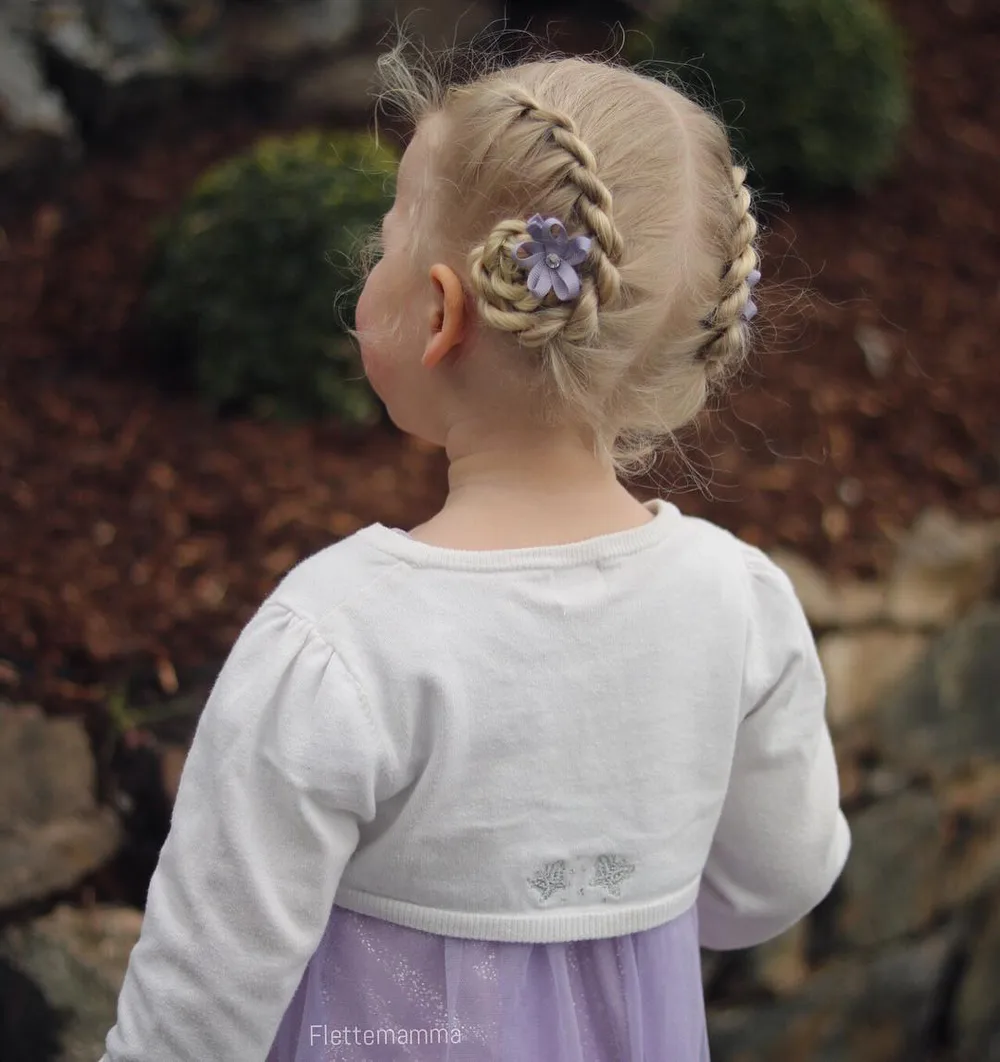 Petite fille avec deux chignons torsadés ornés de petites fleurs blanches