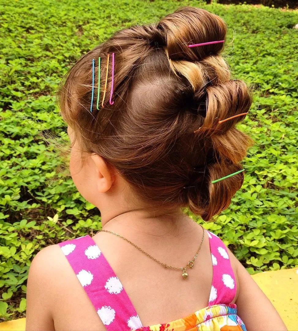 Petite fille avec faux hawk bouclé et pinces colorées, coiffure ludique