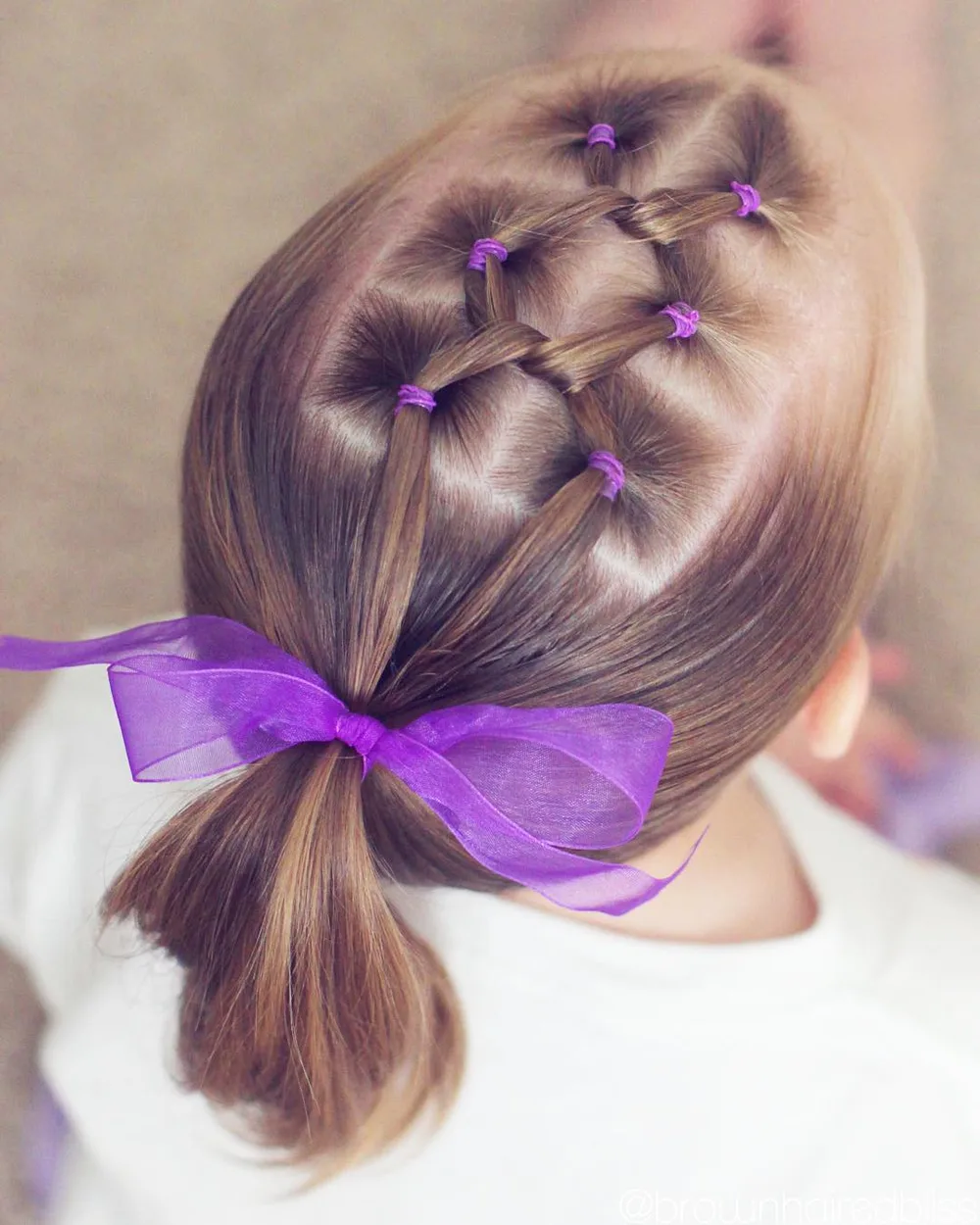 Petite fille avec mini-couettes nouées en croisillons et gros nœud violet