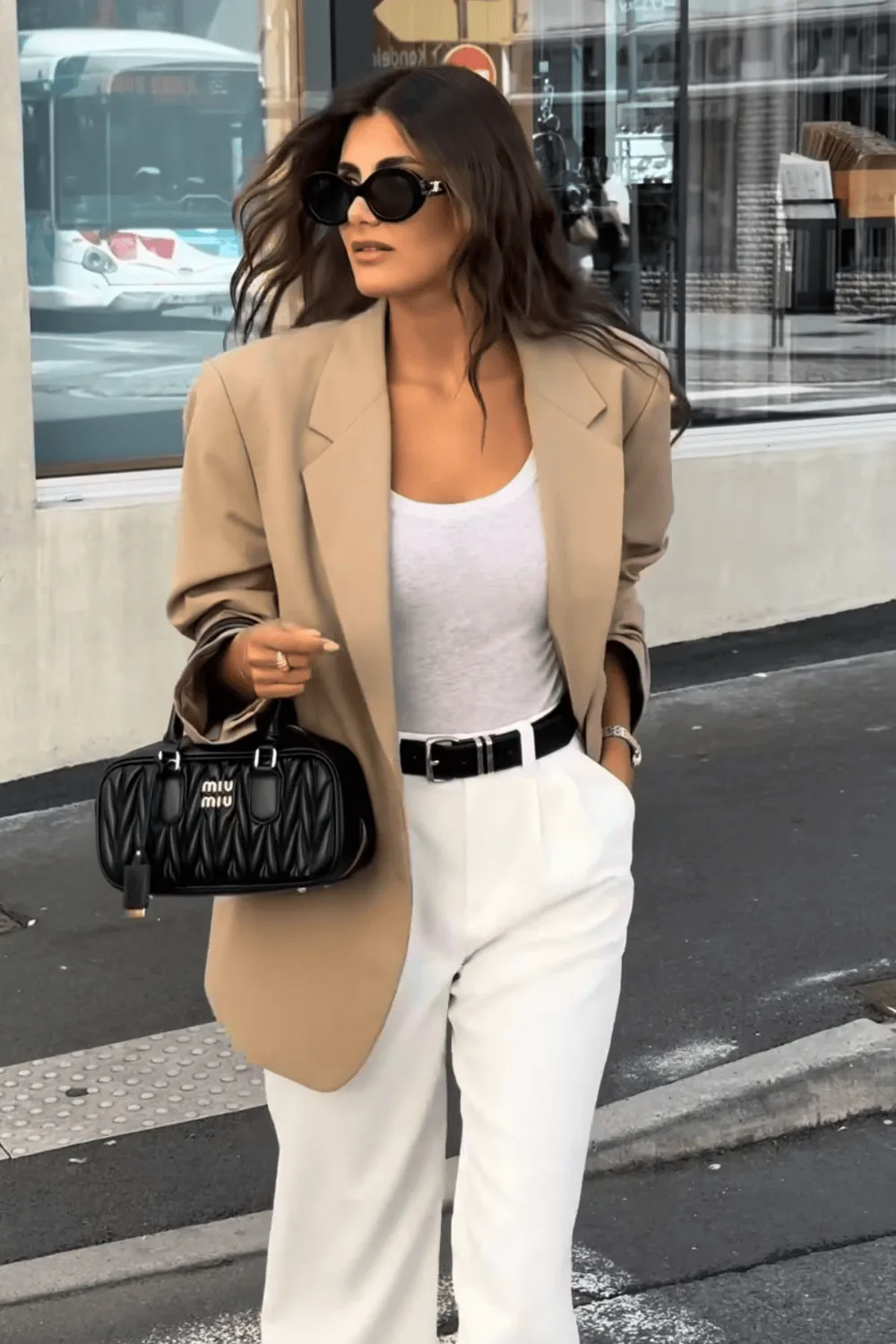 Blazer camel porté sur un débardeur blanc avec un pantalon blanc et une ceinture noire