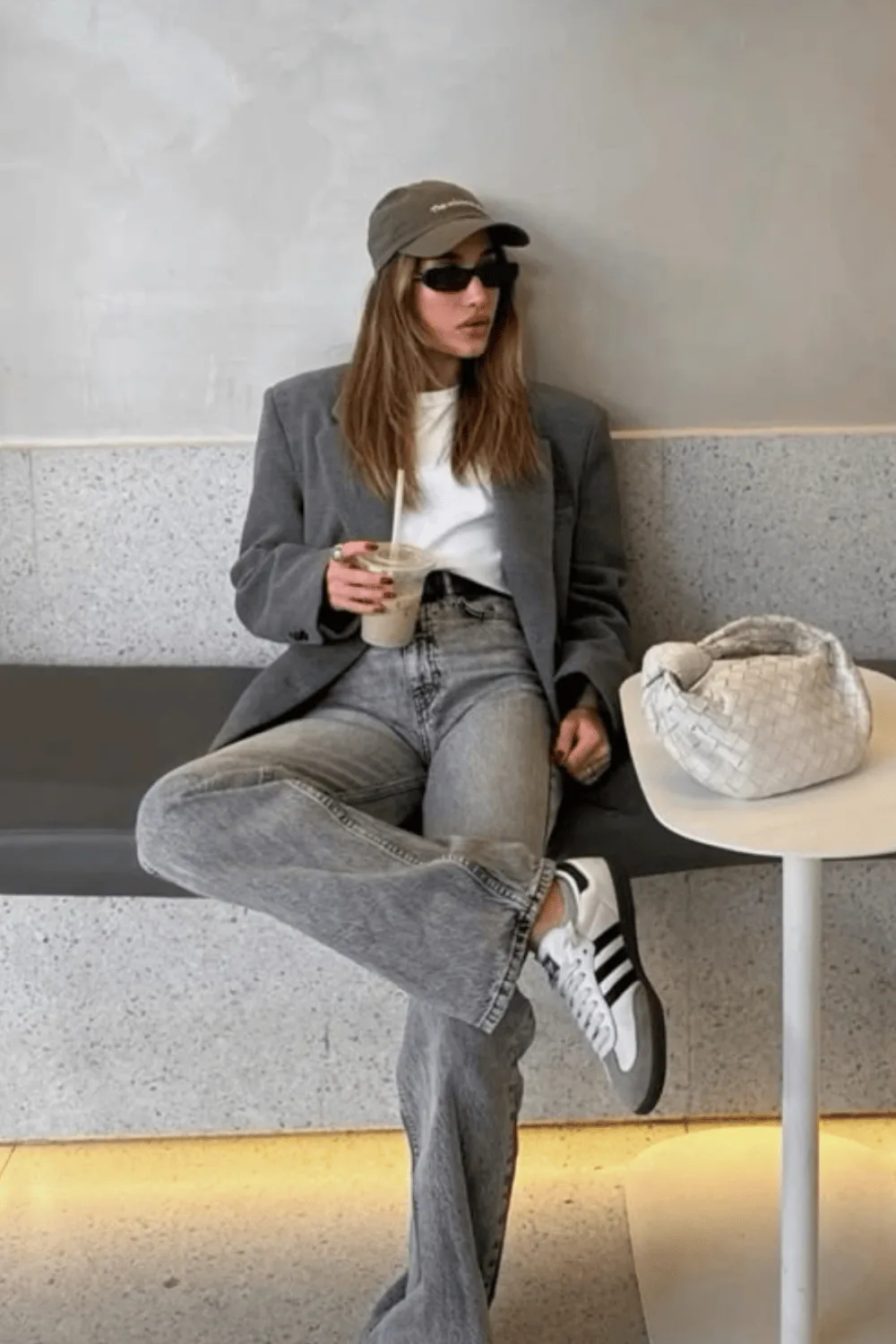 Blazer gris porté avec un jean gris et des baskets, assise sur un banc