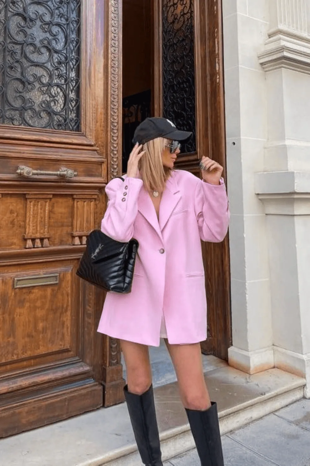 Blazer rose oversize porté avec une casquette noire et des bottes hautes noires