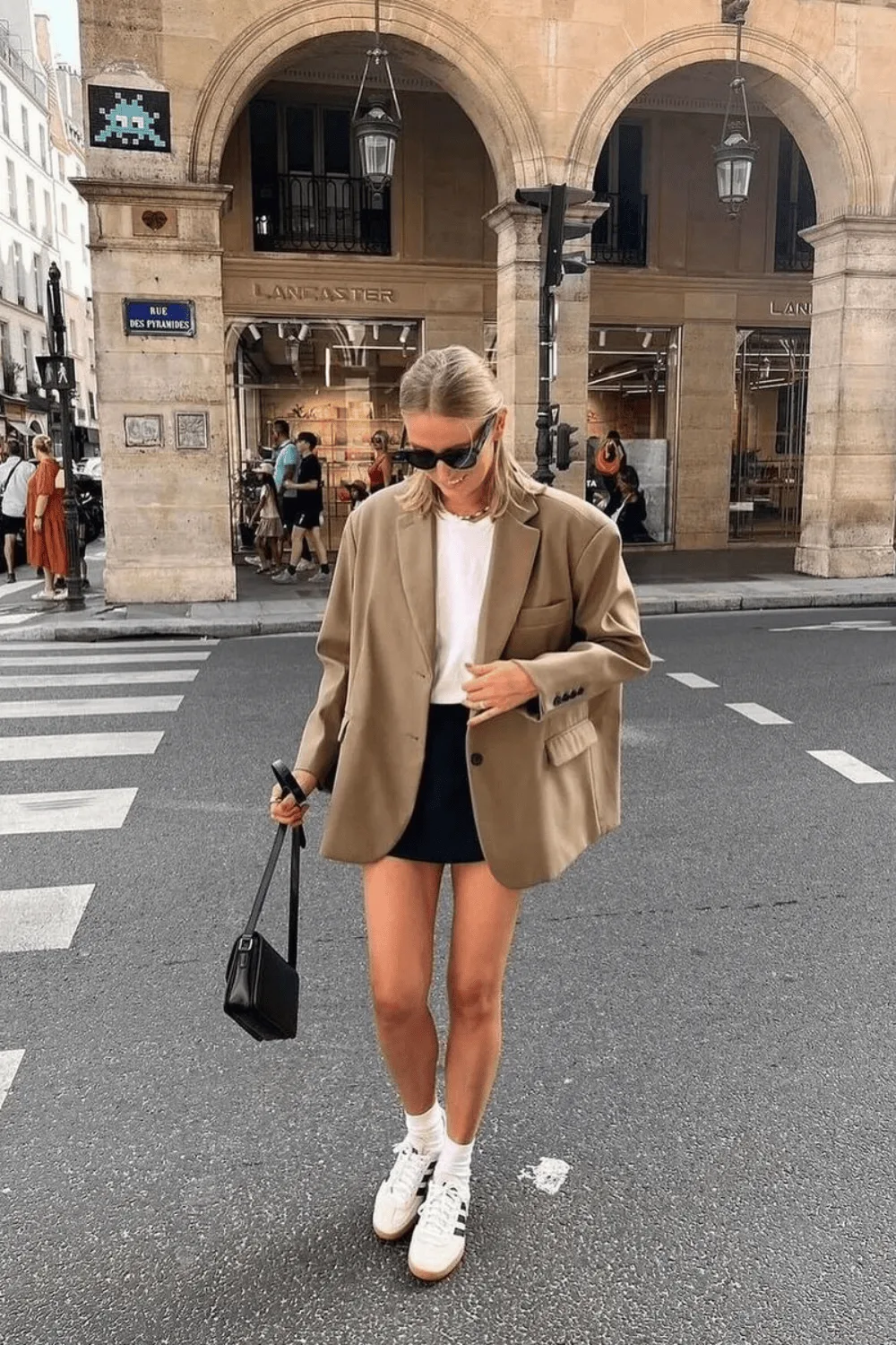 Blazer tan oversize porté avec une mini-jupe noire et des baskets blanches