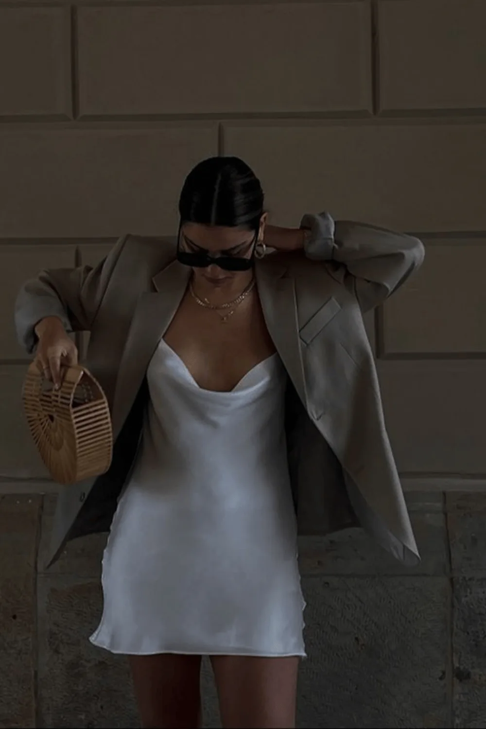 Blazer taupe porté négligemment sur une robe nuisette en satin blanc