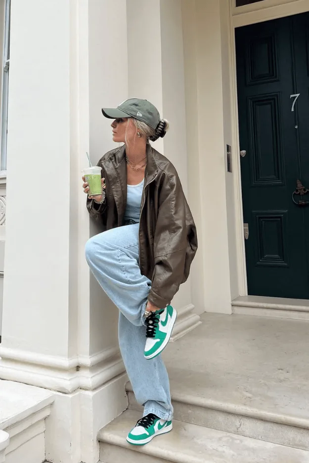 Blouson en cuir marron porté avec un jean clair, des baskets et une casquette