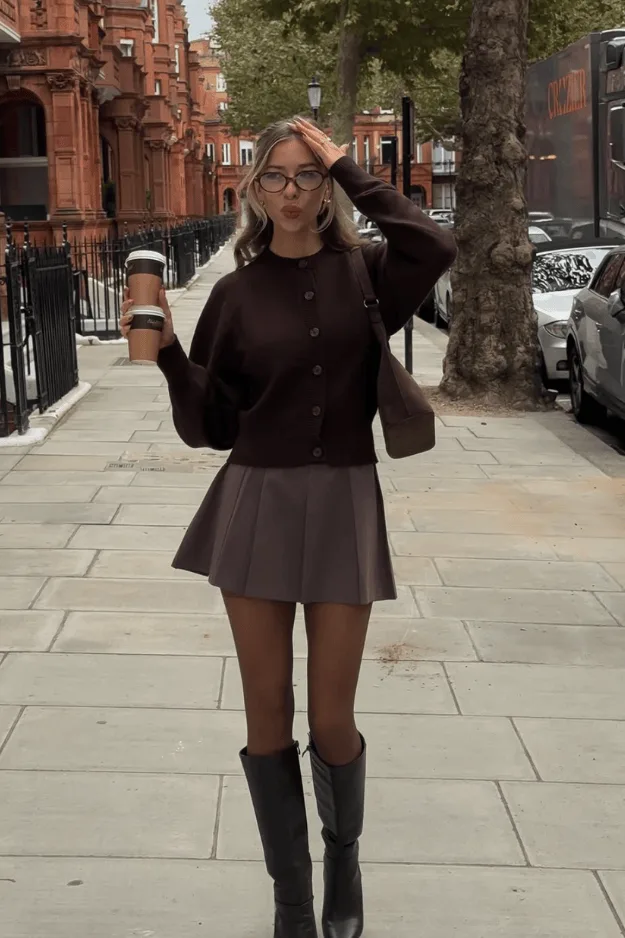 Blouson marron porté avec une mini-jupe en cuir et des bottes hautes