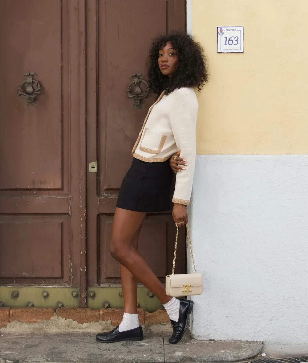 Cardigan crème et jupe noire portés avec des socquettes blanches et des mocassins noirs