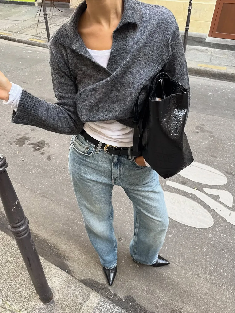 Cardigan gris boutonné porté sur un top blanc avec jean délavé et sac noir