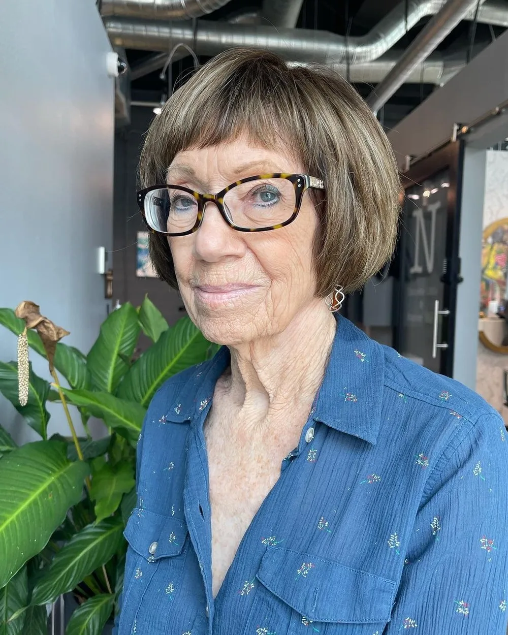 Carré court gris à frange sur femme de 60 ans avec lunettes