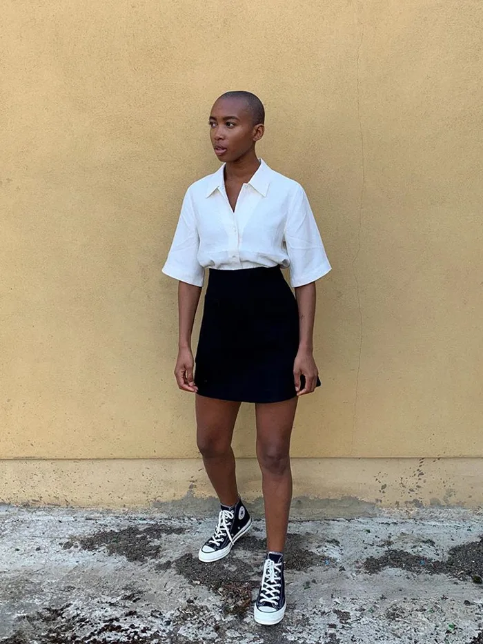 Chemise blanche portée avec une mini-jupe noire et des Converse